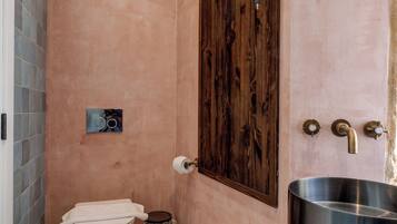 Un bagno con una porta di legno massiccia, un water bianco, un lavandino in acciaio inox e un piccolo cestino.