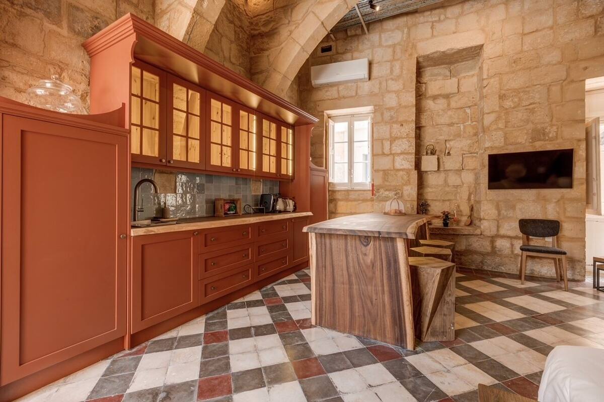 A rustic kitchen with stone walls, wooden cabinets, and a checkered floor.