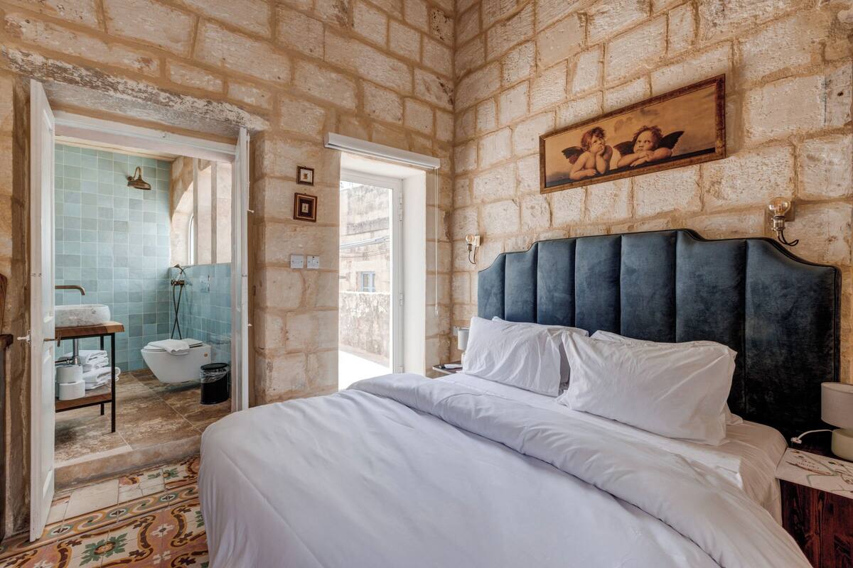 A bedroom with a large bed, a headboard, and a bathroom visible through an open door.