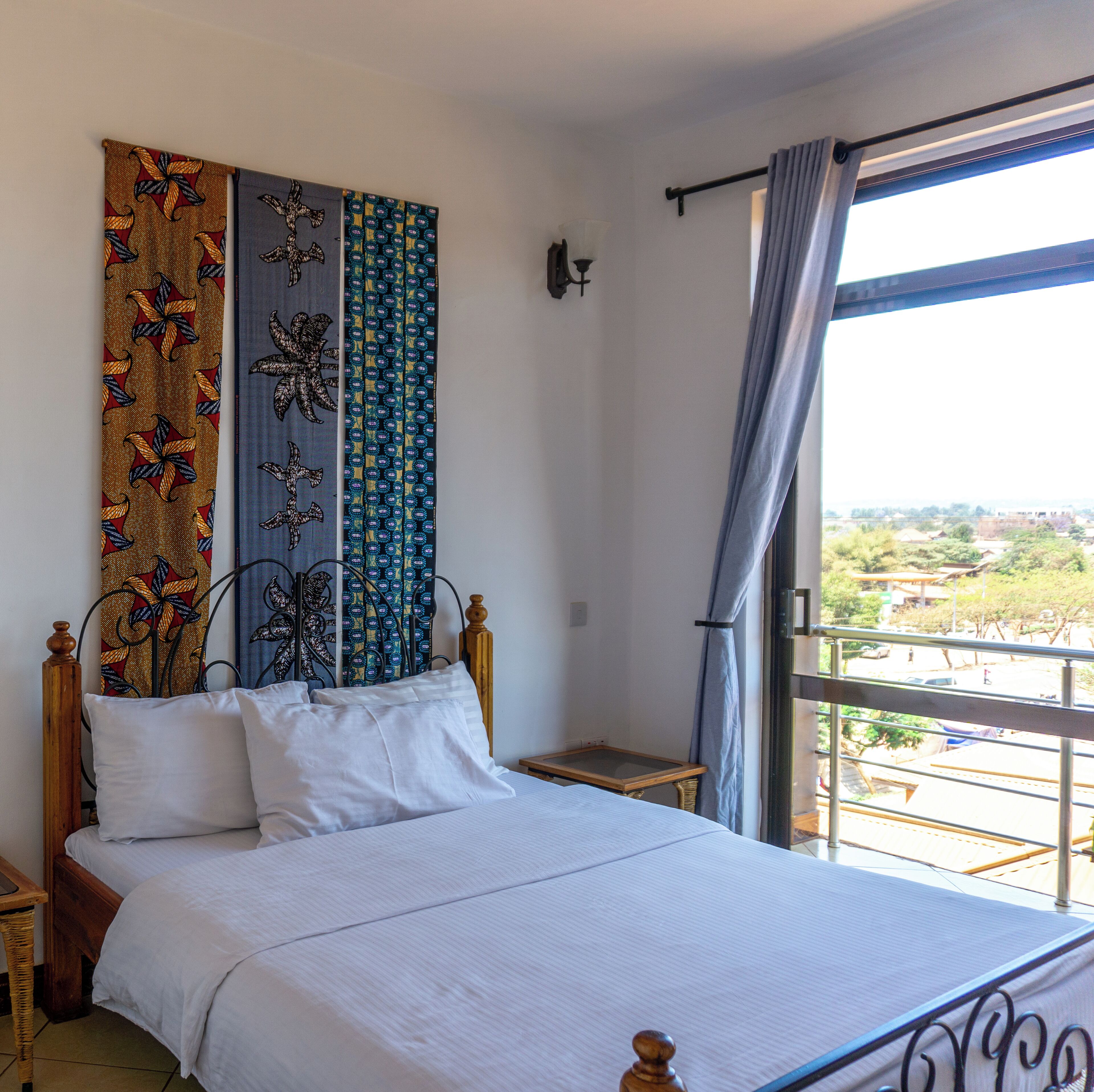 Un dormitorio con cama, mesita de noche, lámpara de pared y ventana con cortinas.