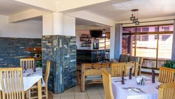 Un restaurante con mesas y sillas de madera, paredes de piedra y una zona de bar con estantes llenos de botellas.
