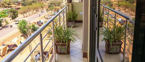 A balcony with potted plants, a metal railing, and a view of a distant landscape.