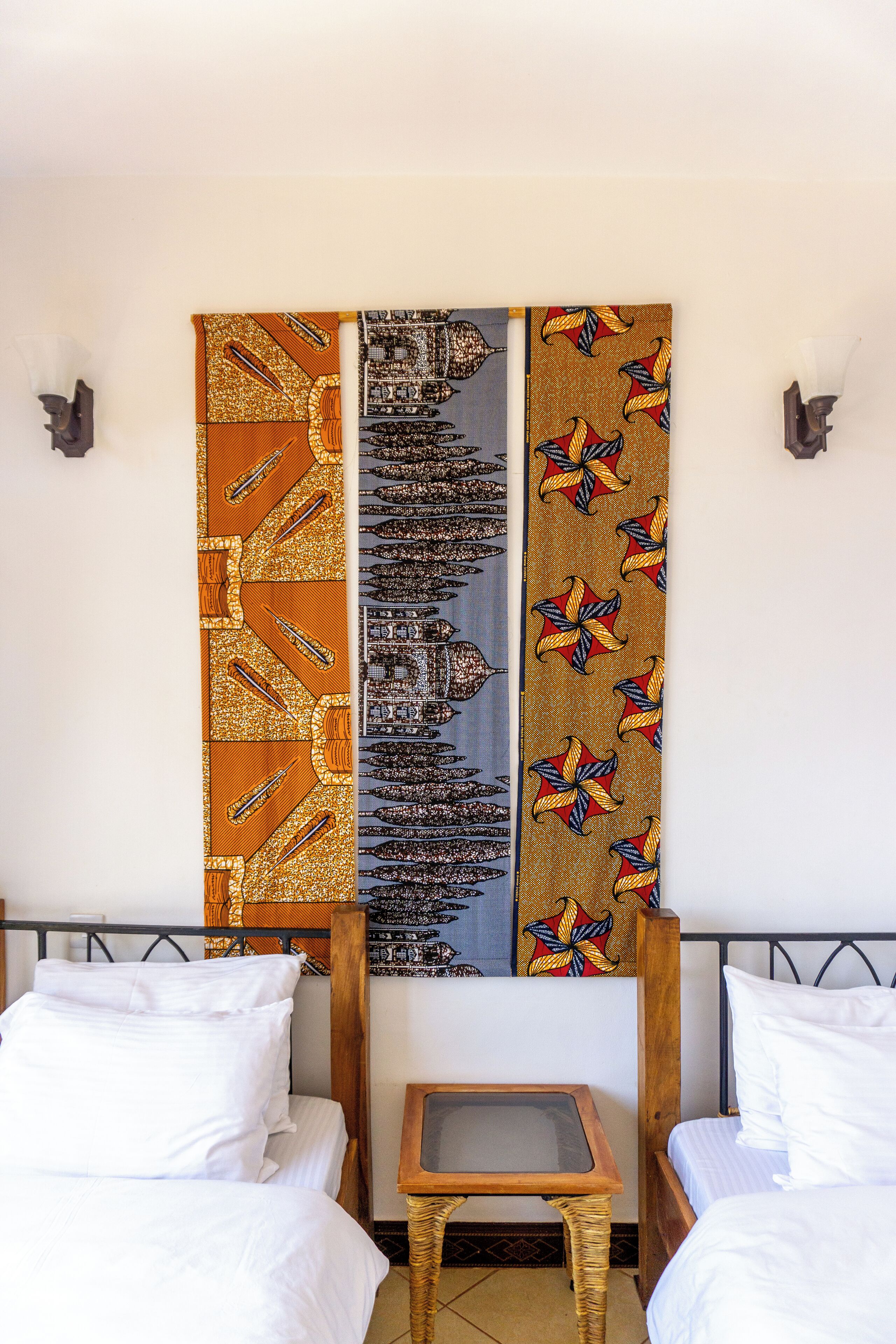 Una habitación con dos camas, una mesita pequeña y una pared decorada con tapices estampados.