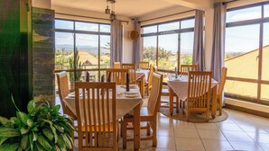 Un espace repas avec des tables et des chaises en bois, de grandes fenêtres avec des rideaux et une vue sur le paysage.