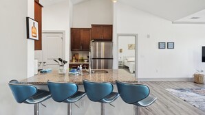 A modern kitchen with a central island, stainless steel appliances, and blue bar stools.