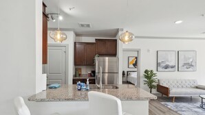 A modern kitchen with granite countertops, stainless steel appliances, and white cabinetry. There is a dining area with white chairs and a small table. - Overlook 7207 I Modern and Spacious 2Bd Apt (Knoxville)