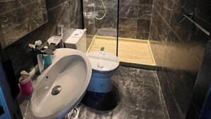 A modern bathroom with a marble floor, a glass-enclosed shower, a white sink, and a mirror.