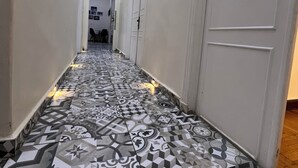 A hallway with patterned floor tiles, white walls, and framed pictures on the walls.