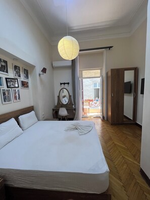 A hotel room with a large bed, a desk with a chair, a mirror, and a wardrobe.