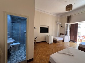 A hotel room with a bathroom, a bed, a TV, and a sliding door to a balcony.