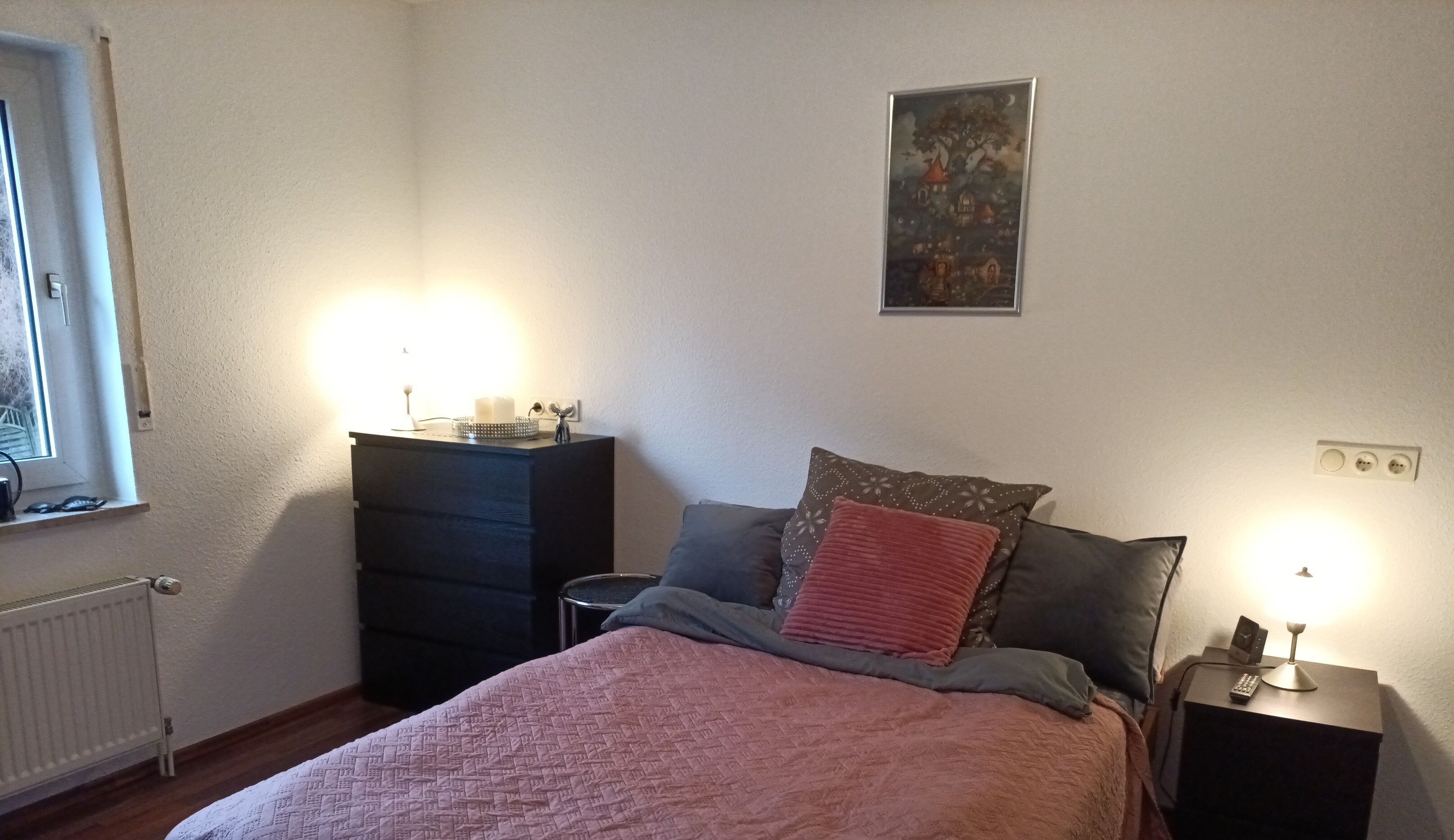 A bedroom with a bed, a dresser, a nightstand, a window, and a wall-mounted picture.