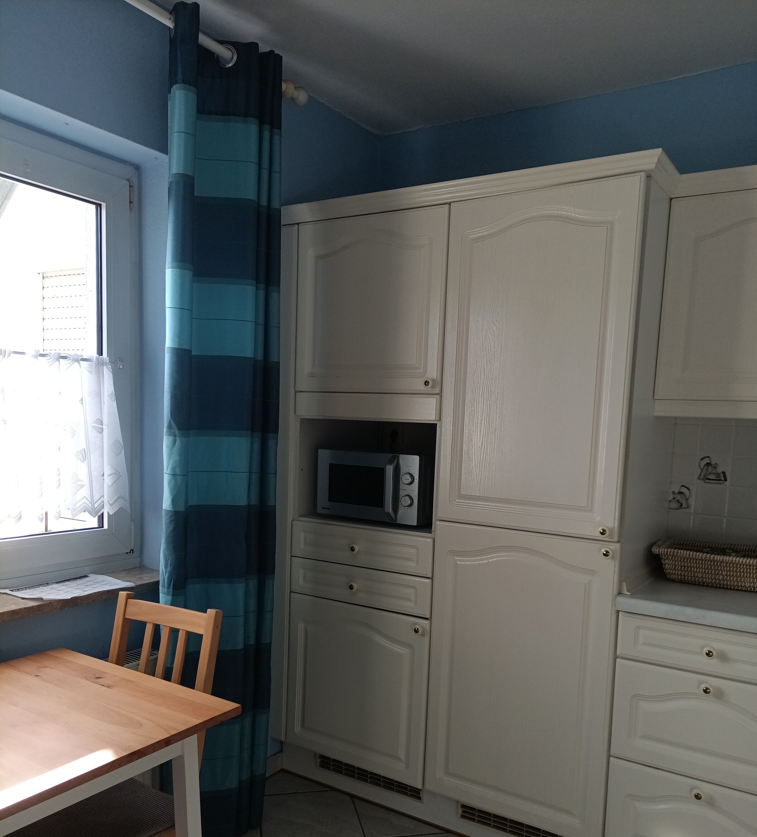 A kitchen with white cabinets, a microwave, and a window with curtains.