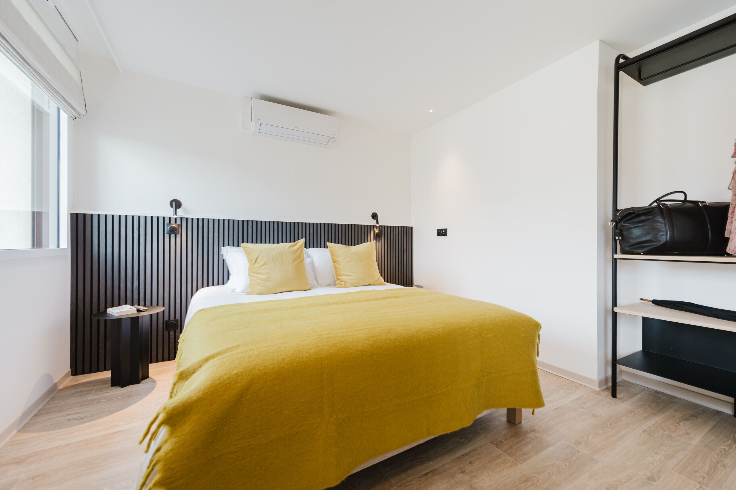 Una habitación de hotel moderna con cama, mesitas de noche, armario y ventana.