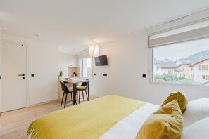 A modern bedroom with a bed, a desk, and a chair. There is a window with a view of buildings and mountains. - 108 - Appart'Hôtel Neostelia-Annecy (Annecy)