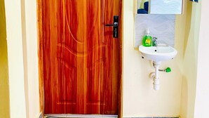 Eine Holztür mit Schlüsselloch, ein weißes Waschbecken mit Spiegel darüber und ein Paar Flip-Flops auf dem Boden.