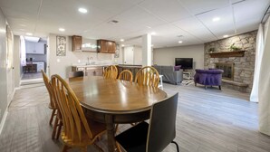 Een ruime woonkamer met een houten eettafel en stoelen, een keuken op de achtergrond en een stenen open haard.