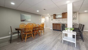 Een ruime eethoek met een houten tafel en stoelen, een witte console en een keuken met houten kasten en een aanrecht.