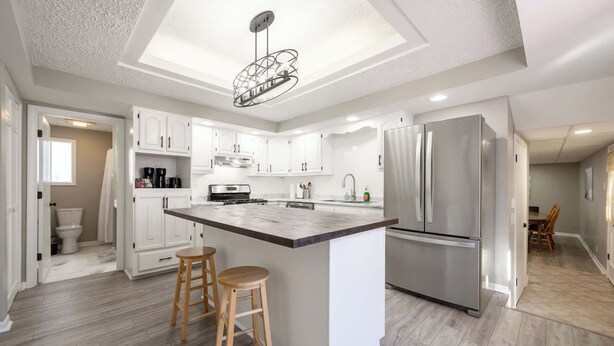 Een moderne keuken met witte kastjes, een centraal eiland met krukken, een roestvrijstalen koelkast en een hanglamp.