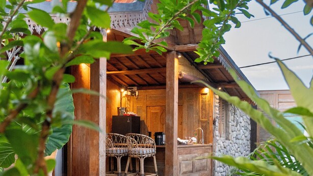 Zona junto a la piscina con terraza de madera, pared de piedra y espacio de descanso con sillas de mimbre.
