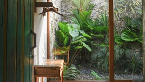 Una habitación con techo de madera, pared de piedra y un gran ventanal con plantas tropicales.