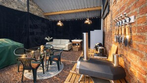 Ein gemütlicher Innenraum mit Essbereich, einer Couch, einem Grill und einer Backsteinwand mit hängenden Werkzeugen.