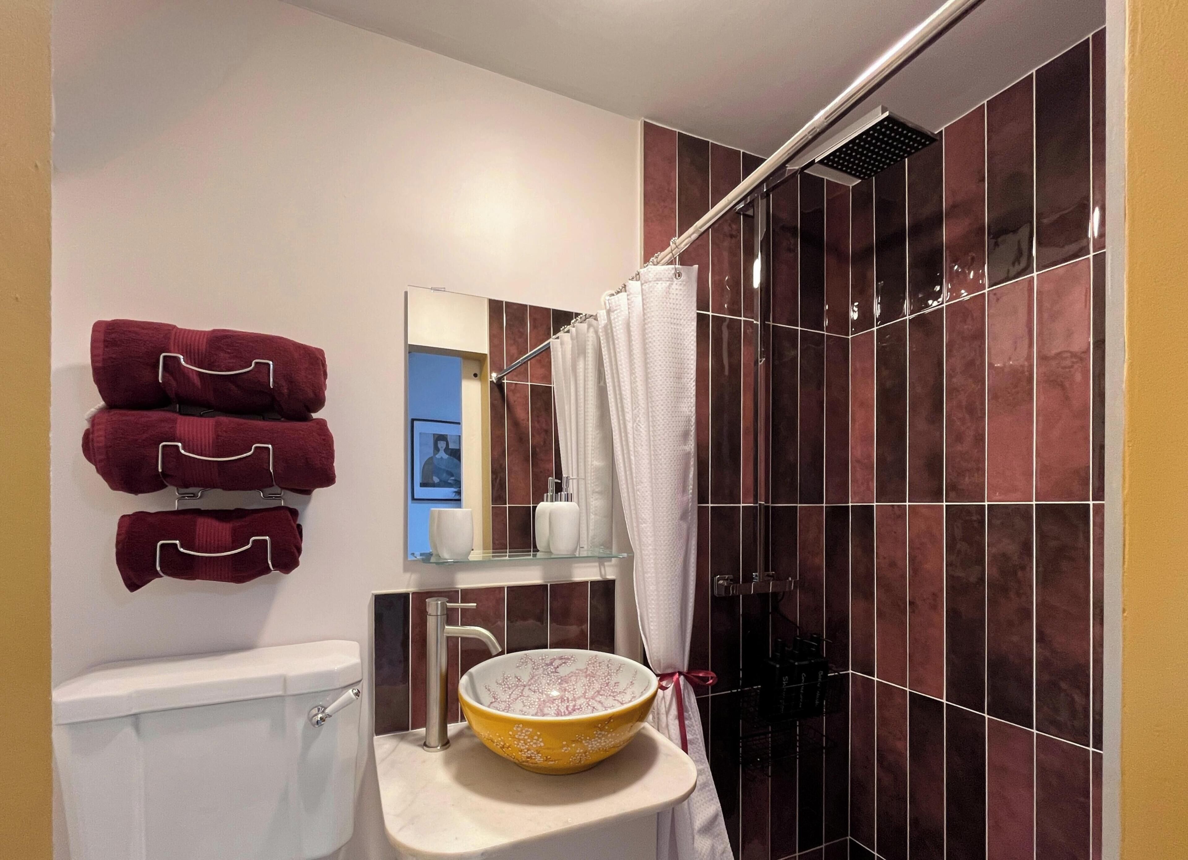 Een badkamer met toilet, een wastafel met decoratieve kom, een douche met gordijn en een spiegel met een lijst eromheen.
