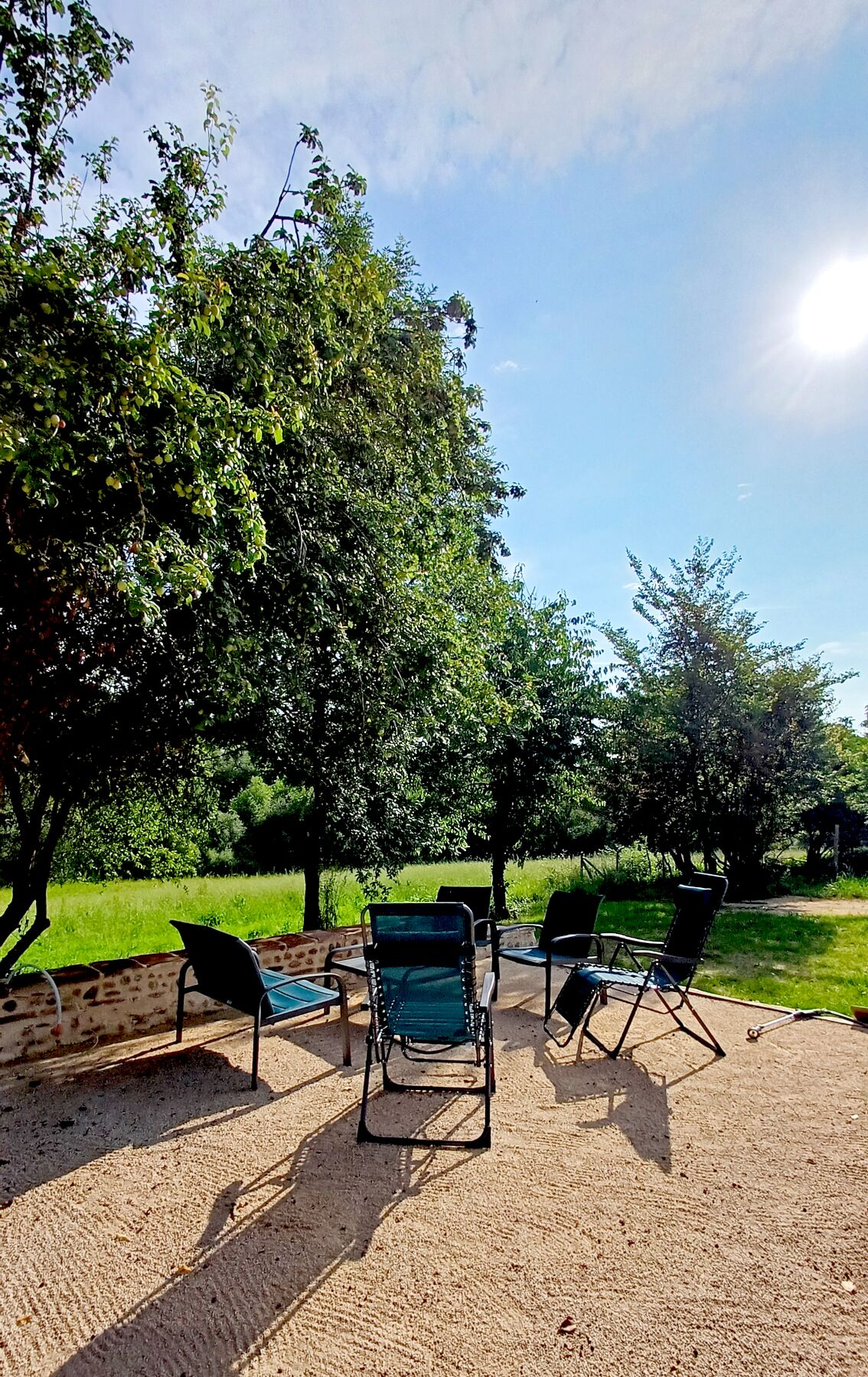 Un espace extérieur aménagé avec trois chaises et une table, entouré d’arbres et d’un champ d’herbe.