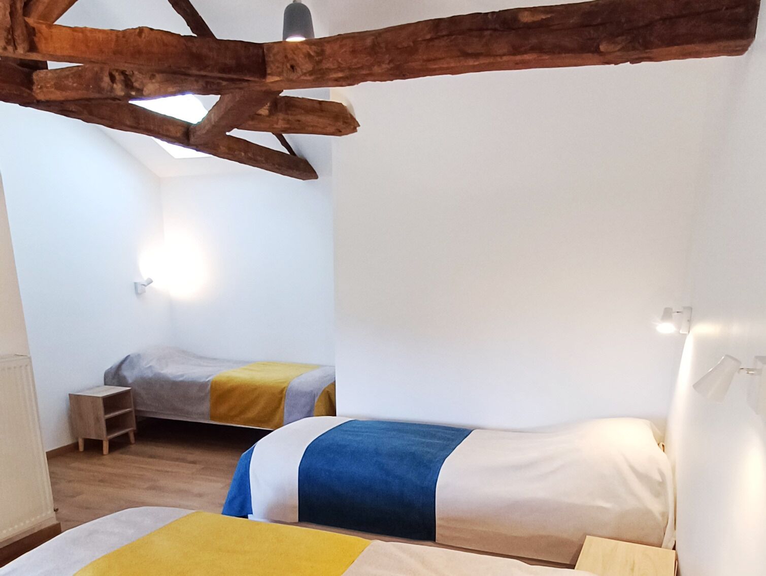 Ein Schlafzimmer mit zwei Betten, Holzbalken, einer kleinen Holzablage und einer Wandleuchte.