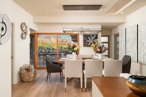 A dining area with a table set for four, a large window with a mountain view, and a wall with abstract art. - Red Rock Luxe Villa: Pool, Spa, Views, Private Courtyard (Sedona)