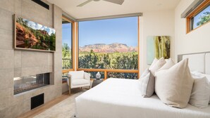 Ein Schlafzimmer mit einem großen Bett, einem an der Wand montierten Fernseher und Blick auf eine gebirgige Landschaft durch große Fenster.