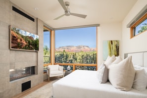 A bedroom with a large bed, a TV mounted on the wall, and a view of a mountainous landscape through large windows. - Red Rock Luxe Villa: Pool, Spa, Views, Private Courtyard (Sedona)
