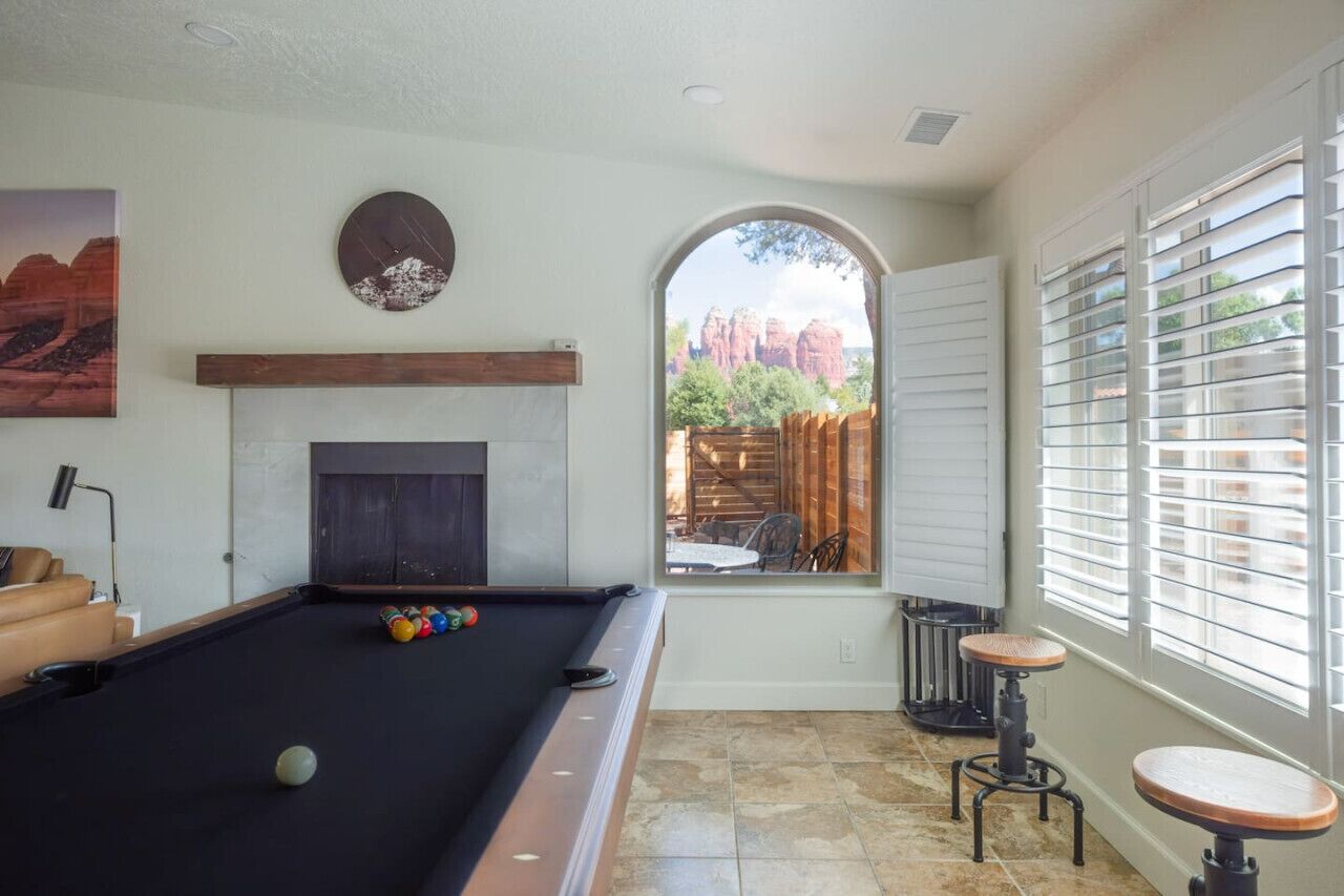A pool table with balls, a fireplace, and a window with a view of red rock formations.