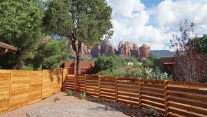A wooden fence, a paved patio, and a large tree in a desert landscape with red rock formations in the background. - Thunder Mtn, Coffee Pot Views, Hot Tub Getaway (Sedona)