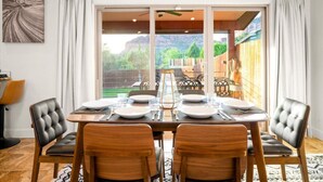 A dining area with a table set for two, large windows with curtains, and a view of the outdoors. - Thunder Mtn, Coffee Pot Views, Hot Tub Getaway (Sedona)