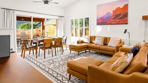 A spacious living room with a large sectional sofa, a dining area with wooden chairs, and a large window with blinds. - Thunder Mtn, Coffee Pot Views, Hot Tub Getaway (Sedona)