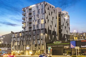 A modern multi-story building with a geometric facade, a prominent sign for a business, and a visible entrance.