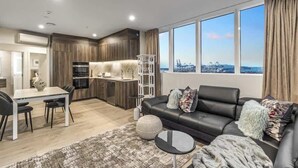 Una sala moderna con un sofá de cuero negro, una mesa de comedor con sillas y una zona de cocina con armarios de madera y una isla blanca.