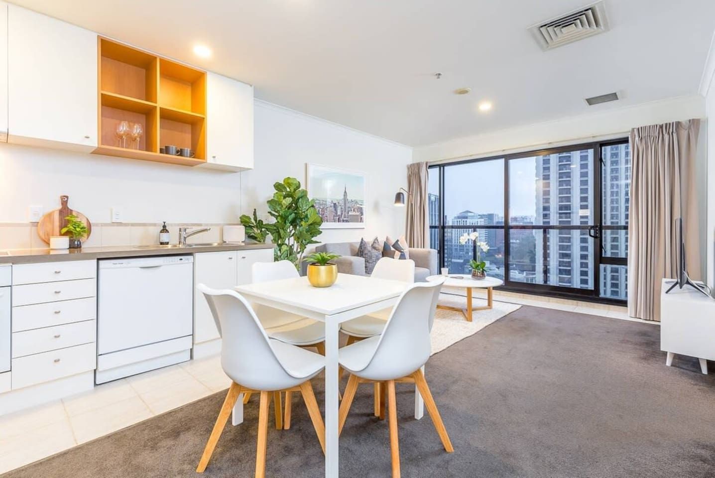 A modern apartment with a dining area, kitchen, and large windows offering city views.