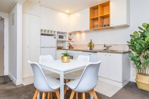 A compact kitchen with white cabinetry, a dining table with chairs, and a potted plant. - Stylish Apt with Views Pool and Gym - Zodiak Stays (Auckland)