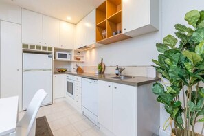 A modern kitchen with white cabinetry, a built-in microwave, a sink, and a countertop with a plant. - Stylish Apt with Views Pool and Gym - Zodiak Stays (Auckland)