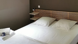 Un lit bien fait, avec du linge de lit blanc, une tête de lit en bois et un luminaire mural en forme de soleil.