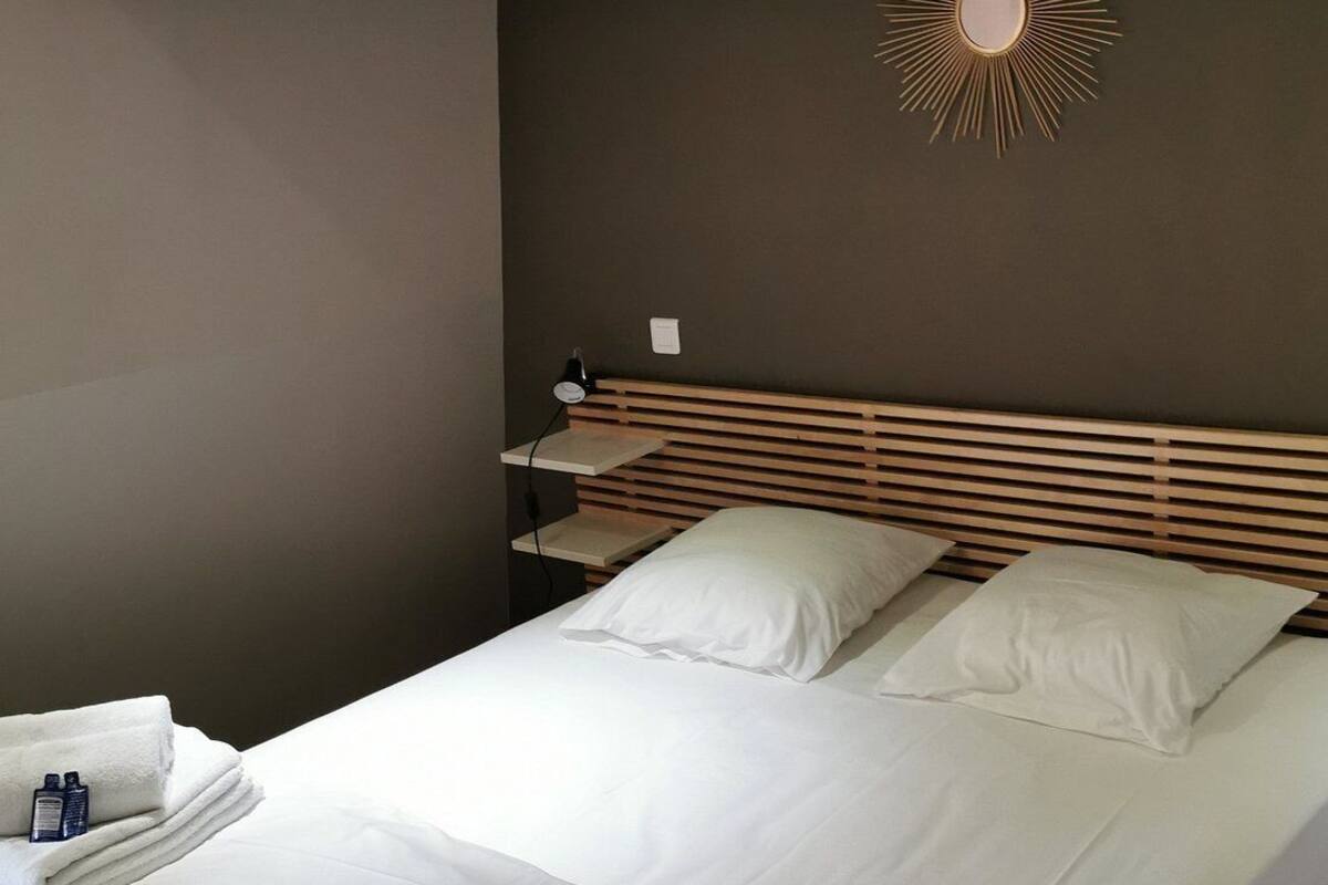 Een opgemaakt bed met witte lakens, een houten hoofdbord en een zonlichtarmatuur aan de muur.