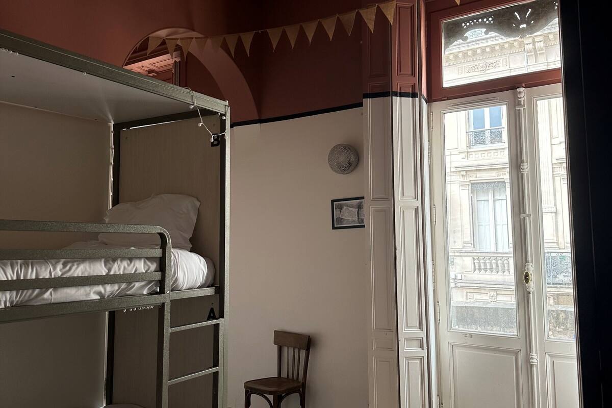 Een kamer met een stapelbed, een stoel, een deur naar buiten en een houten vloer met een patroon.