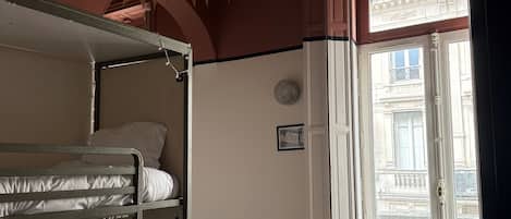 Una habitación con una cama litera, una silla, una puerta que da al exterior y un suelo de madera con diseño.