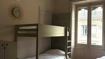 Ein Zimmer mit Etagenbetten, einem Kleiderschrank, einem Zier-Spiegel und einem Fenster mit Blick auf Gebäude.