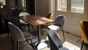 Un coin repas avec une table en bois et quatre chaises, une plante en pot, et une vue sur un bâtiment à travers une porte vitrée.