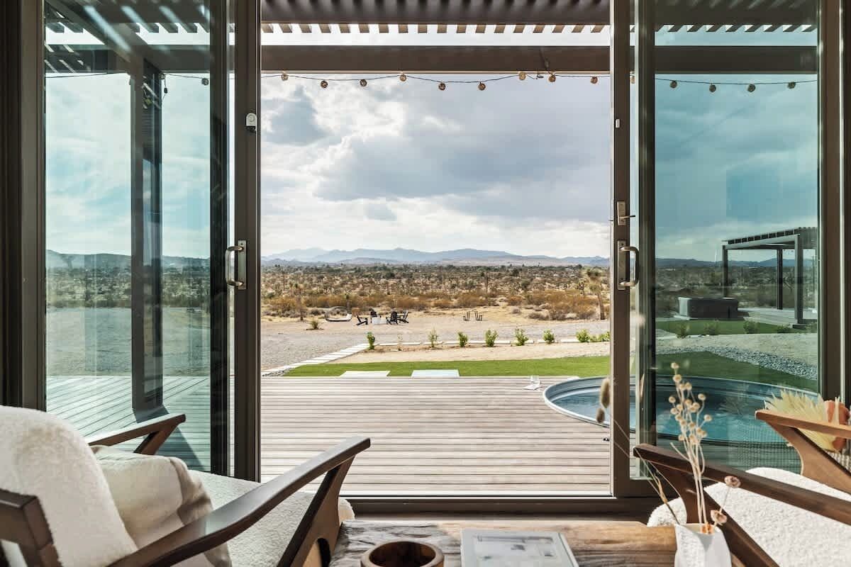 Ein modernes Zimmer mit großen Glasüren, einer Holzterrasse und Blick auf eine Wüstenlandschaft.