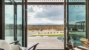 A modern room with large glass doors, a wooden deck, and a view of a desert landscape.