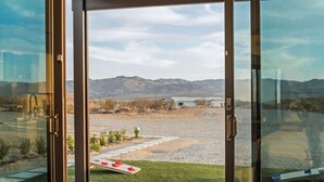 A view from a room with large glass doors to an outdoor area with a gravel path, a small lawn, and distant mountains.