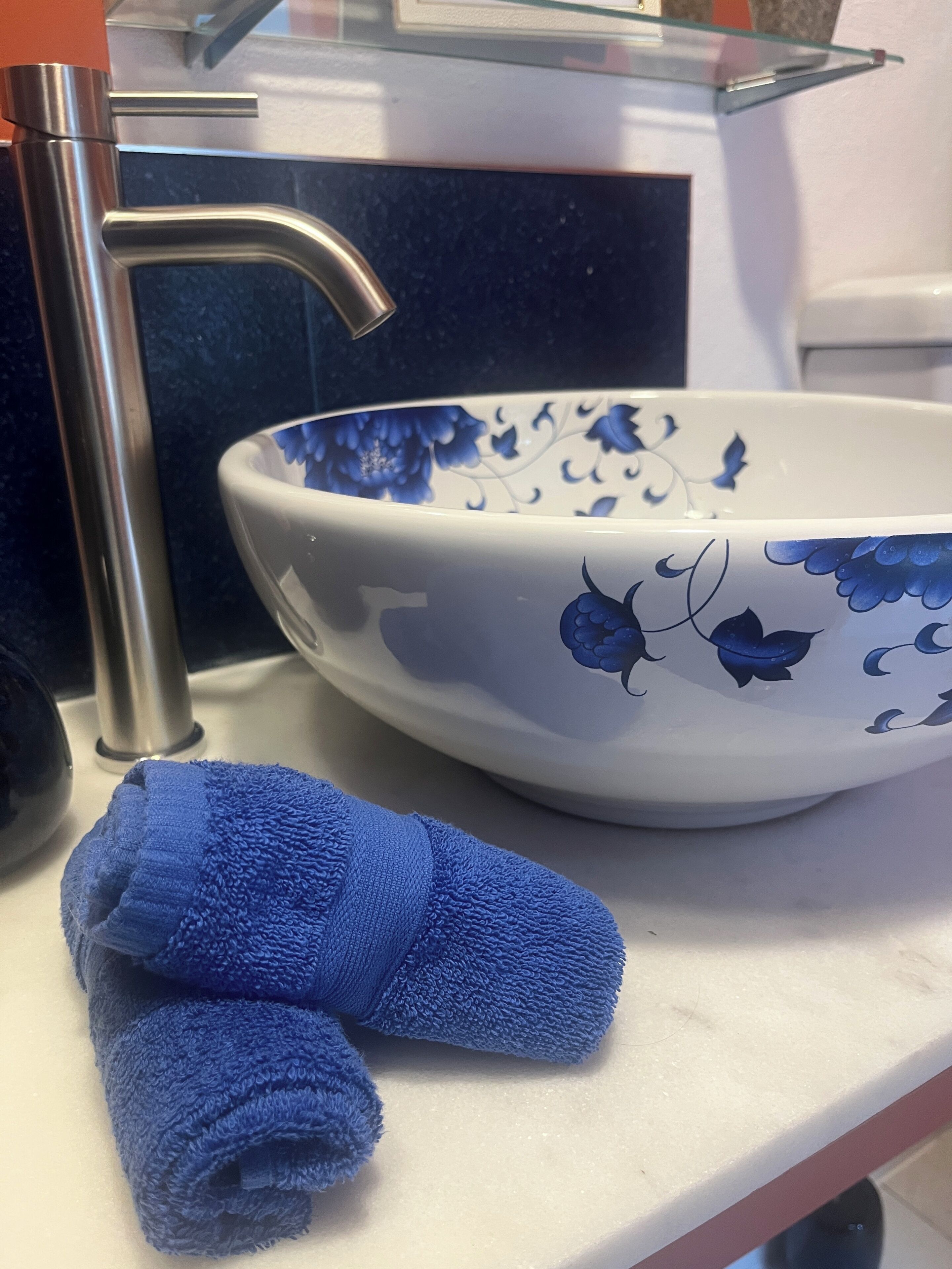 Uma pia de banheiro com cuba azul estampada com flores, uma toalha azul e uma torneira cromada.